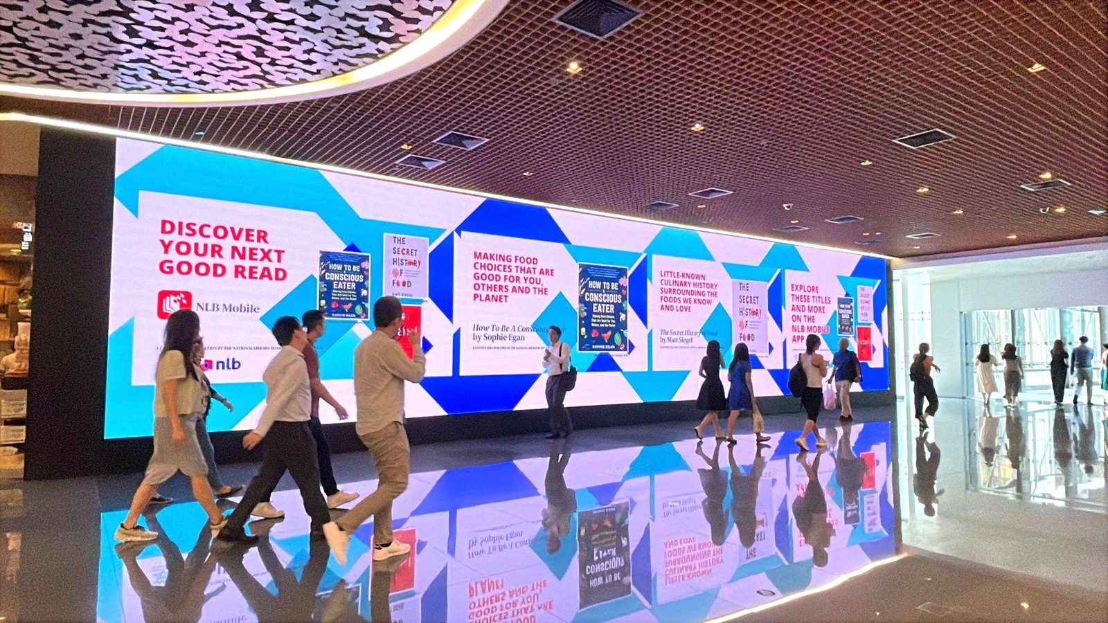 Office workers walking past the Asia Square Tower 1 LED screen to Food Garden